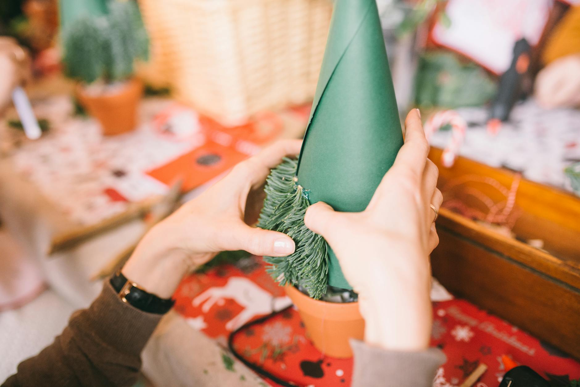 Dłonie robią papierową choinkę z zielonego kartonu i gałązek świerku