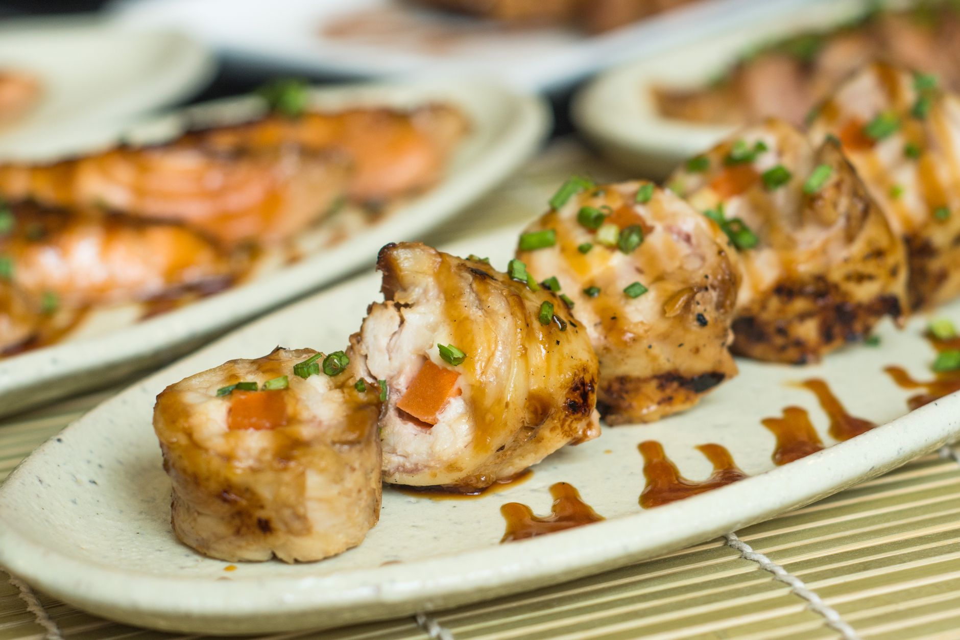 Grillowane rolki sushi z dymką i sosem na jasnym ceramicznym talerzu