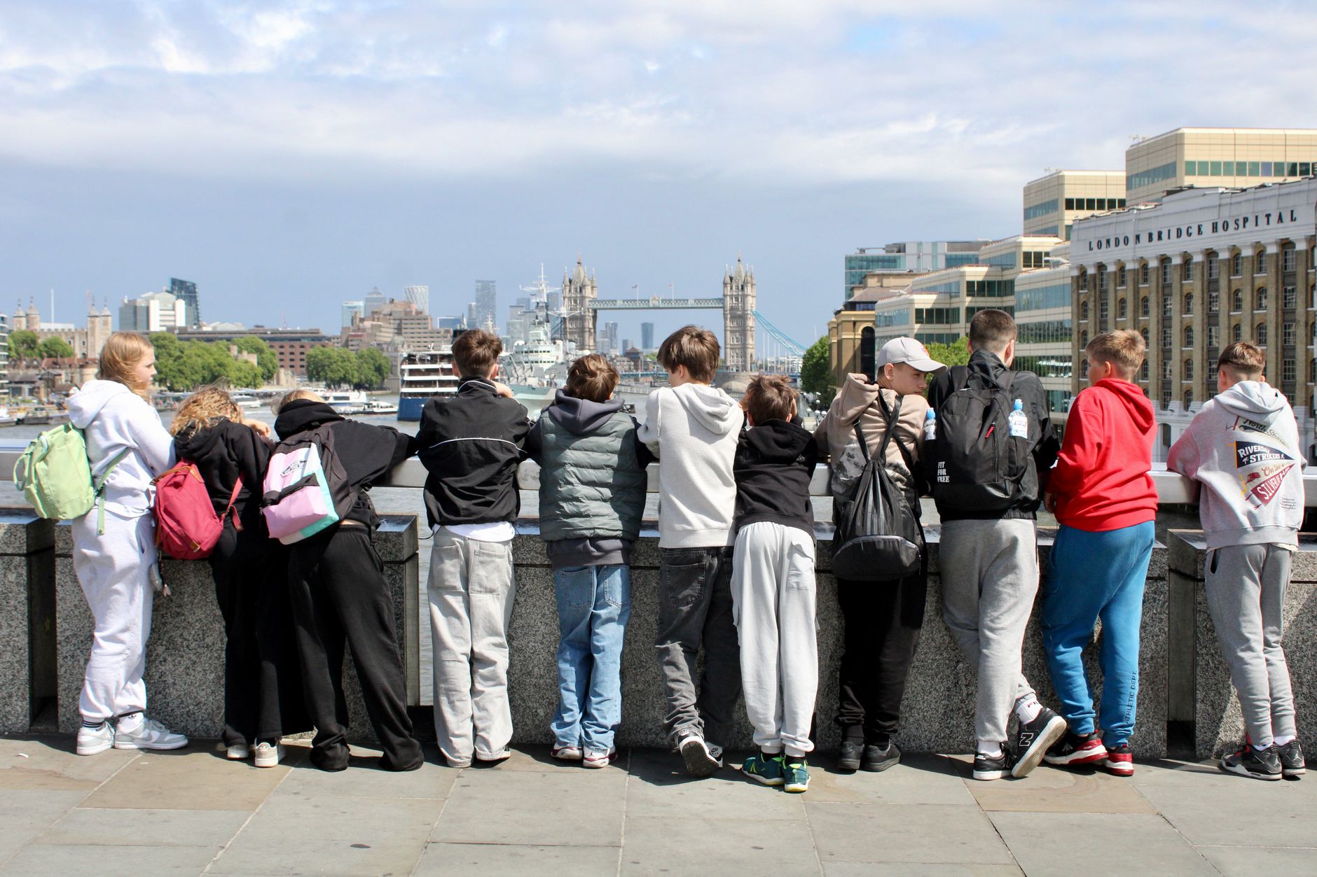 Nastolatki z plecakami patrzą na Tower Bridge znad brzegu Tamizy